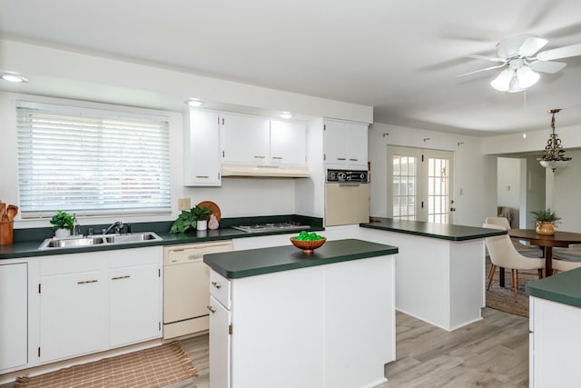 kitchen with a sink, under cabinet range hood, dark countertops, wall oven, and dishwasher