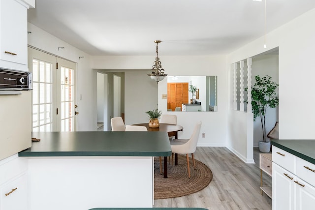 kitchen featuring light wood-type flooring, decorative light fixtures, dark countertops, white cabinetry, and a peninsula