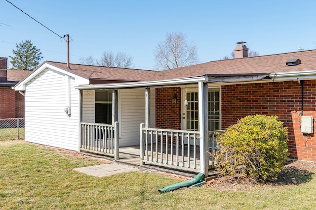 back of property featuring brick siding, fence, a porch, a chimney, and a yard