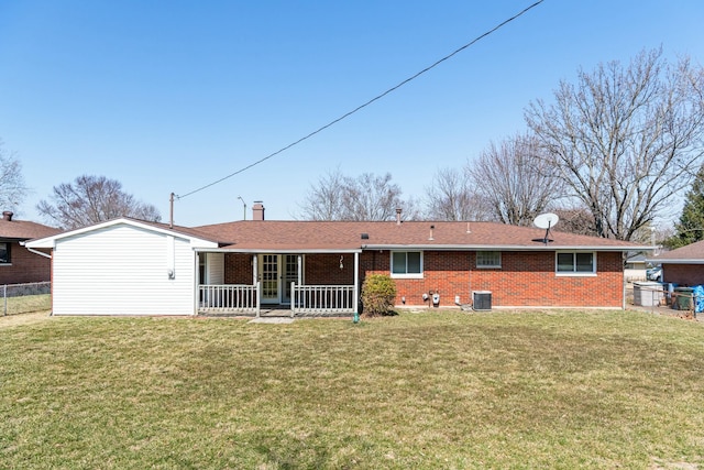 rear view of property featuring brick siding, a chimney, a yard, and fence