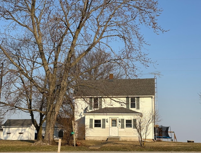 view of front facade featuring a trampoline, a chimney, a front lawn, and a shingled roof