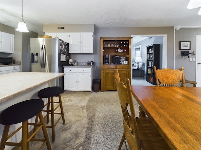 kitchen featuring a breakfast bar, stainless steel fridge with ice dispenser, hanging light fixtures, and white cabinets