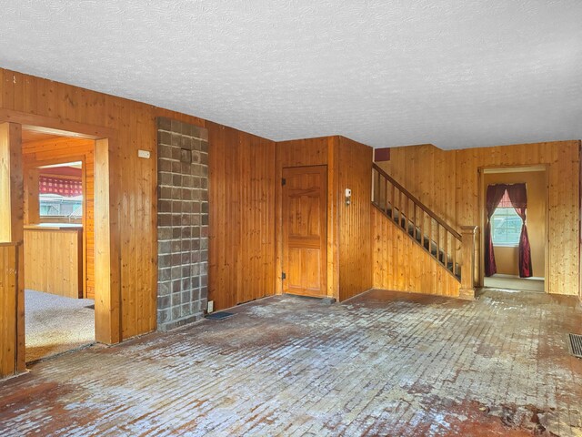 interior space featuring a textured ceiling, stairway, visible vents, and wooden walls
