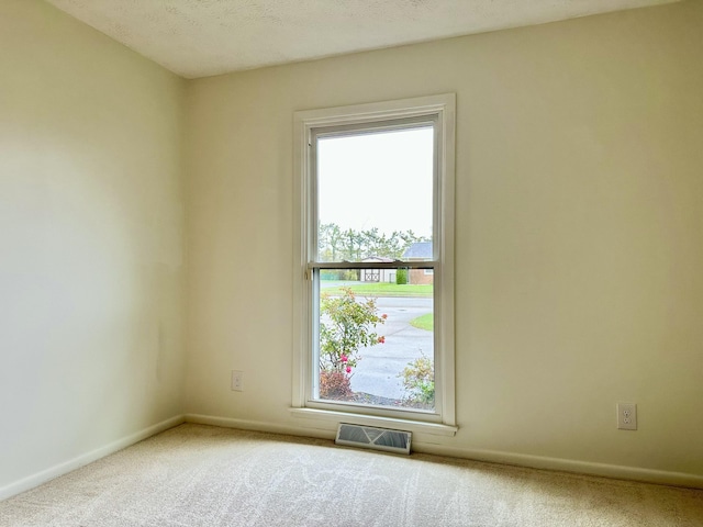 carpeted spare room featuring visible vents, a textured ceiling, and baseboards