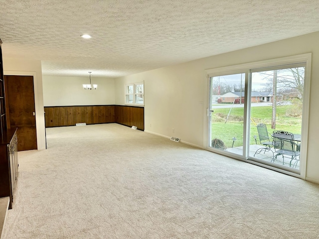 empty room with a chandelier, wainscoting, carpet flooring, and wood walls