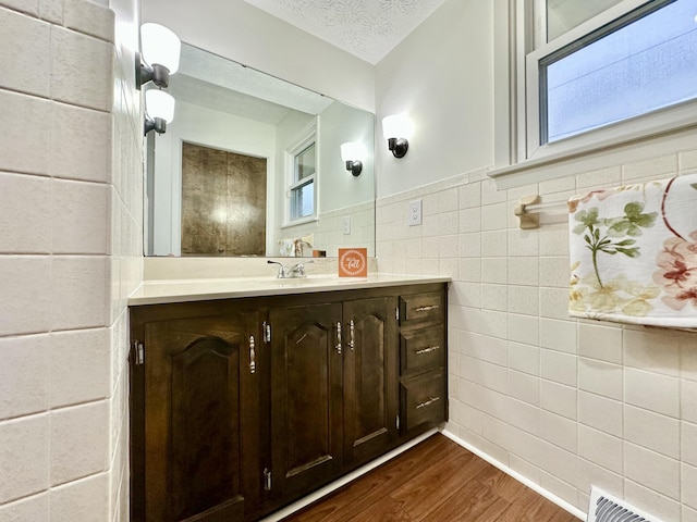 bathroom with a textured ceiling, wood finished floors, vanity, visible vents, and tile walls