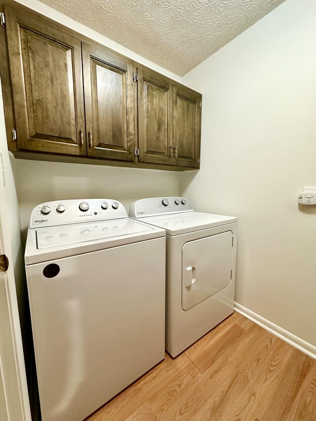 laundry room featuring a textured ceiling, baseboards, light wood-type flooring, cabinet space, and washing machine and clothes dryer