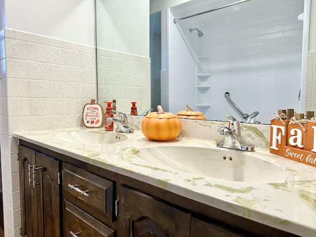 full bath featuring double vanity, a sink, tile walls, and walk in shower