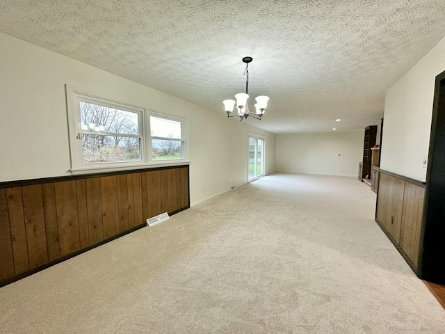 unfurnished room featuring a notable chandelier, a wainscoted wall, wood walls, carpet flooring, and visible vents