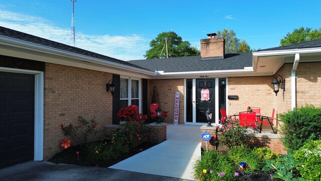 property entrance with a shingled roof, covered porch, brick siding, and a chimney