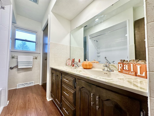 bathroom with wood finished floors, vanity, visible vents, tile walls, and walk in shower