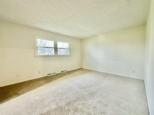 carpeted spare room featuring baseboards, visible vents, and a textured ceiling