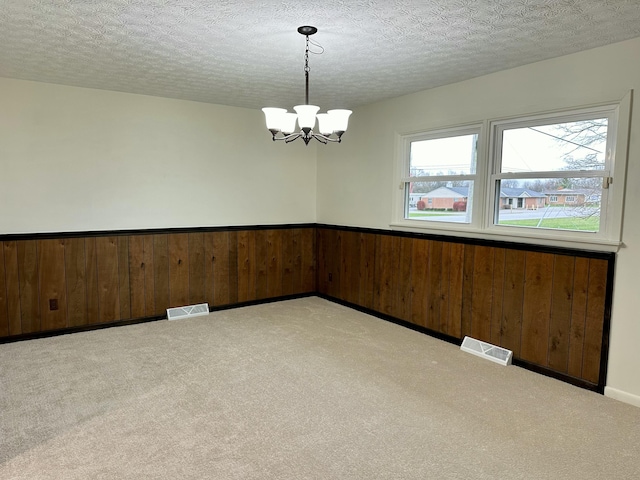 empty room featuring wainscoting, visible vents, a notable chandelier, and carpet flooring