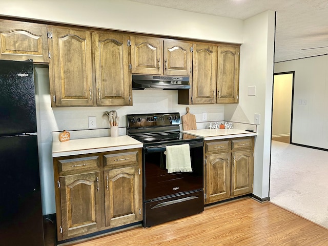 kitchen with light wood finished floors, baseboards, under cabinet range hood, light countertops, and black appliances