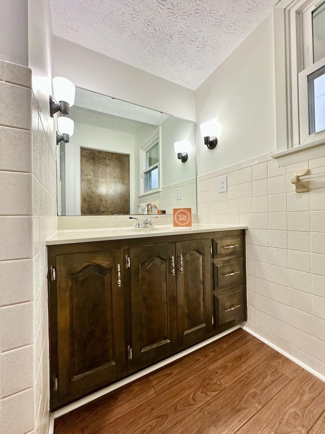 bathroom featuring a textured ceiling, wood finished floors, vanity, tile walls, and wainscoting