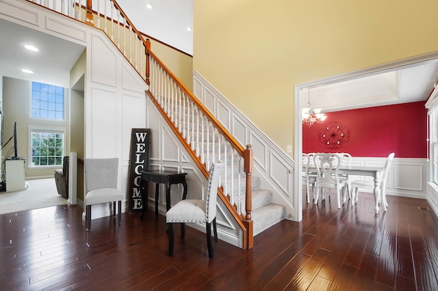 stairs featuring an inviting chandelier, wood-type flooring, and a high ceiling