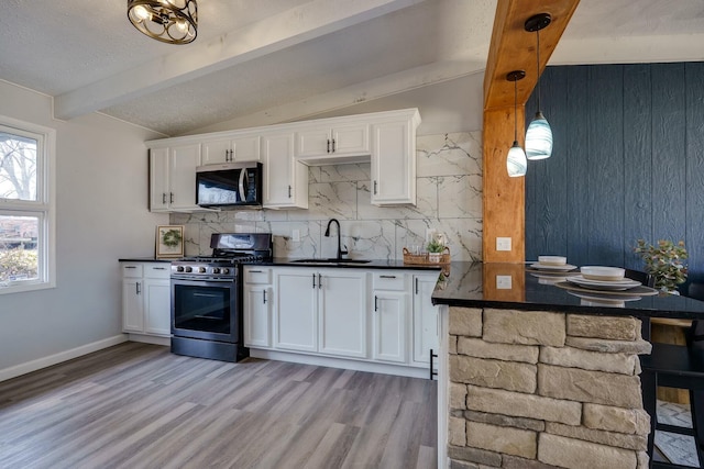 kitchen with lofted ceiling with beams, a sink, stainless steel appliances, white cabinets, and dark countertops