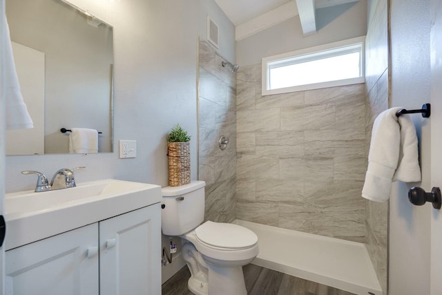 bathroom with visible vents, toilet, a tile shower, wood finished floors, and vanity