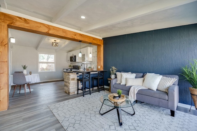 living area with baseboards, wood walls, lofted ceiling with beams, recessed lighting, and wood finished floors