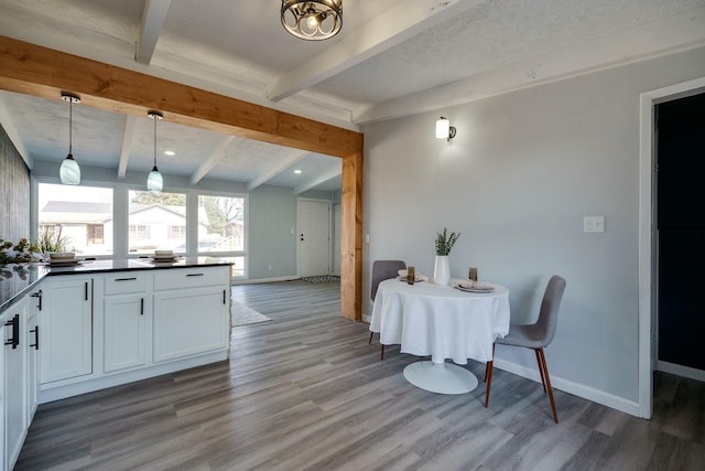 kitchen with wood finished floors, baseboards, beam ceiling, white cabinets, and dark countertops