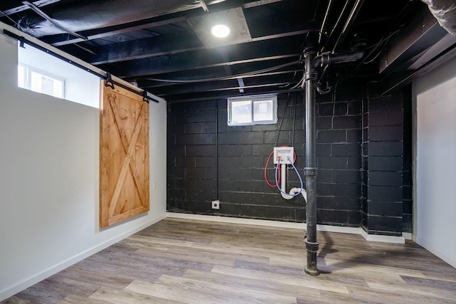 below grade area with baseboards, a barn door, and wood finished floors