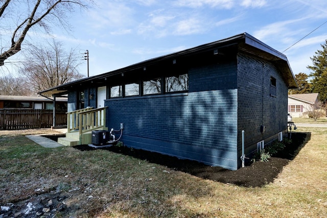 view of property exterior with fence, brick siding, and central AC