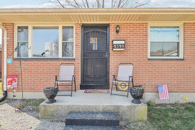 doorway to property with a porch and brick siding