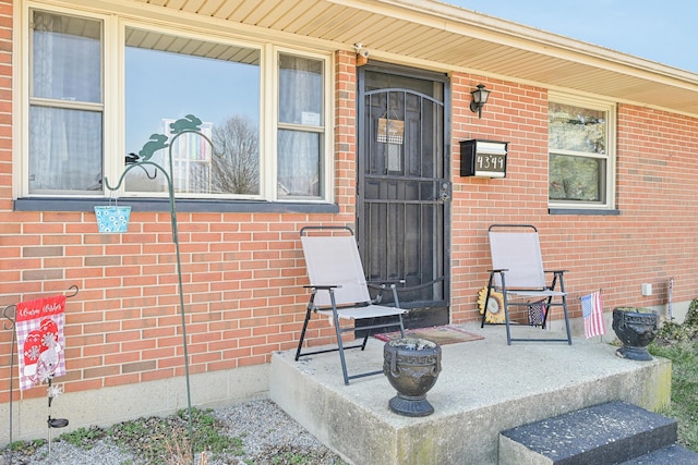 view of exterior entry with brick siding and a porch