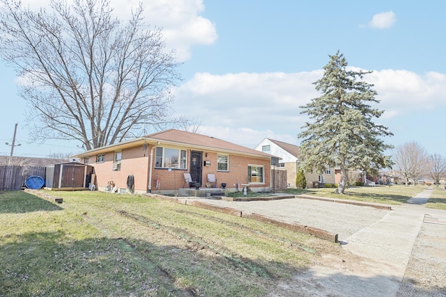 single story home featuring an outbuilding, a front lawn, fence, a storage shed, and brick siding