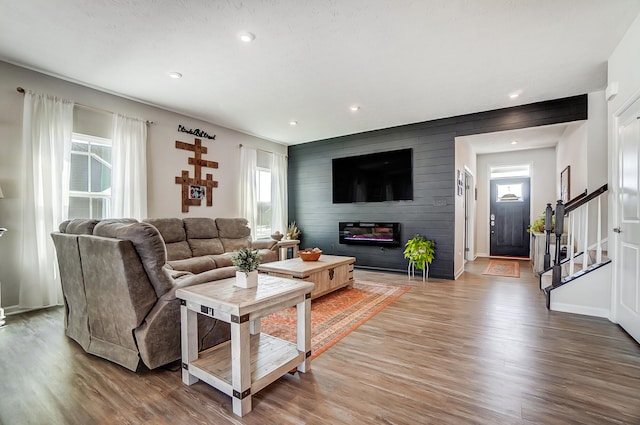 living room featuring stairway, wooden walls, wood finished floors, recessed lighting, and a large fireplace