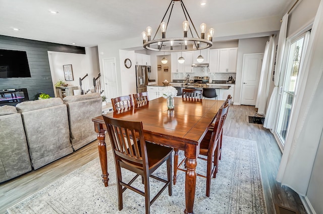 dining space with an inviting chandelier, light wood-style flooring, recessed lighting, wood walls, and an accent wall