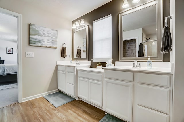 full bathroom with wood finished floors, baseboards, double vanity, a sink, and an enclosed shower