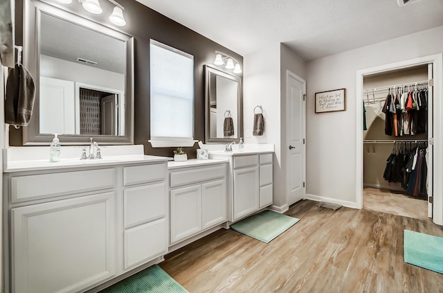 bathroom featuring visible vents, a walk in closet, wood finished floors, double vanity, and baseboards