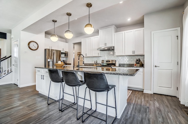 kitchen featuring a sink, under cabinet range hood, a kitchen breakfast bar, backsplash, and stainless steel appliances