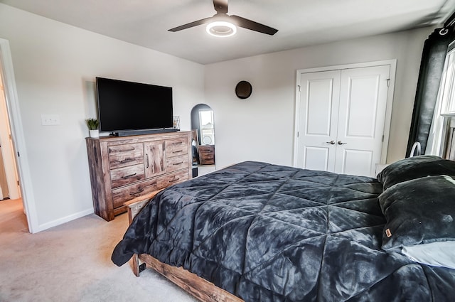 bedroom featuring light carpet, a closet, arched walkways, baseboards, and ceiling fan