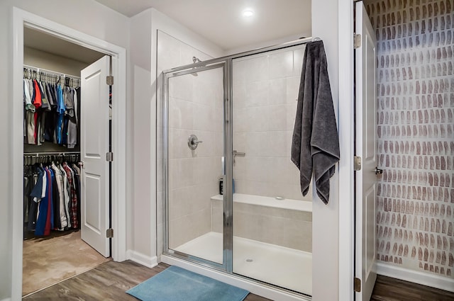 bathroom with a walk in closet, wood finished floors, and a stall shower