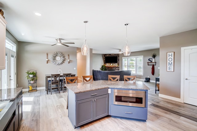 kitchen with stainless steel microwave, light stone counters, pendant lighting, and a center island