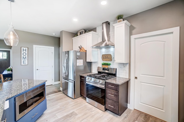 kitchen featuring stainless steel appliances, white cabinetry, light stone countertops, and wall chimney range hood