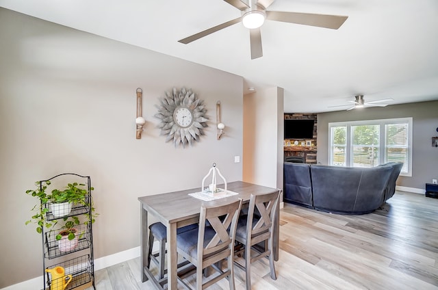 dining area featuring ceiling fan, a large fireplace, and light hardwood / wood-style floors