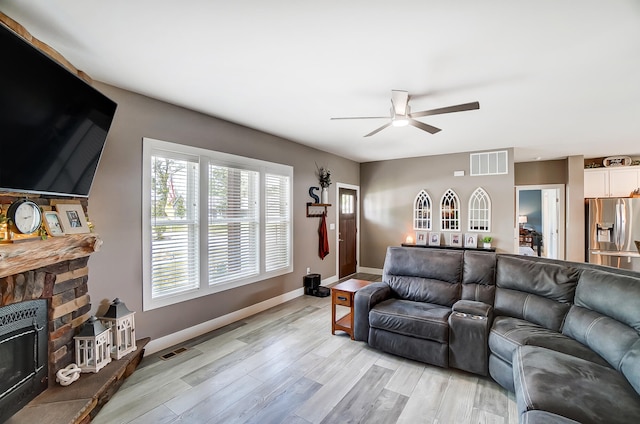 living room featuring a stone fireplace, light hardwood / wood-style floors, and ceiling fan