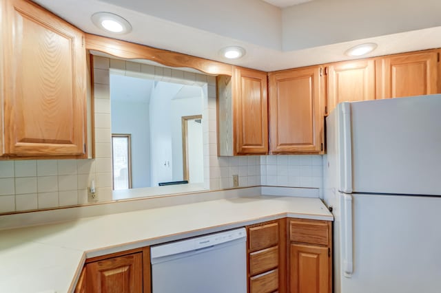 kitchen with brown cabinets, white appliances, tasteful backsplash, and light countertops