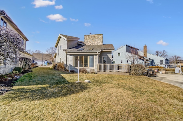 back of house featuring a shingled roof, a chimney, fence, and a lawn