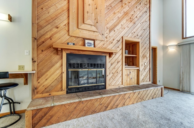 carpeted living area featuring wood walls, a fireplace, a towering ceiling, and baseboards