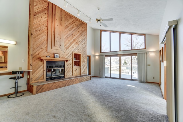 carpeted living room featuring a towering ceiling, baseboards, track lighting, and a glass covered fireplace