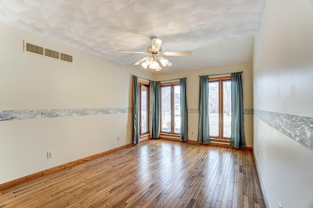 empty room featuring ceiling fan, light wood-style flooring, visible vents, and baseboards