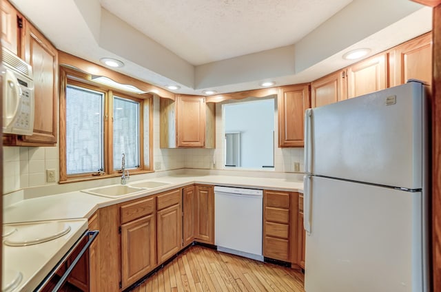 kitchen with light wood finished floors, tasteful backsplash, light countertops, a sink, and white appliances