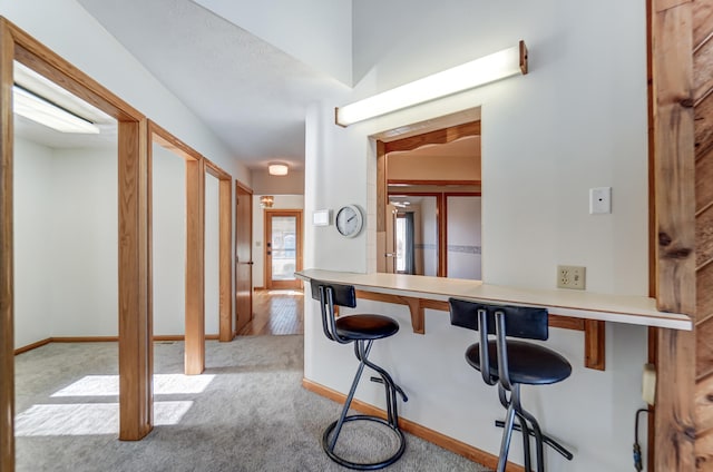 interior space featuring a breakfast bar area, light carpet, and baseboards