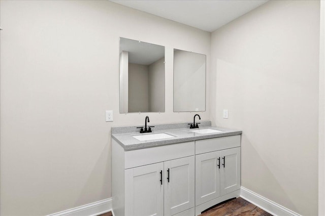 bathroom featuring double vanity, wood finished floors, baseboards, and a sink