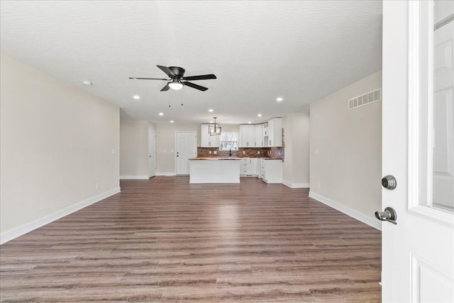 unfurnished living room featuring visible vents, wood finished floors, baseboards, and ceiling fan