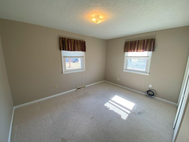 carpeted spare room featuring visible vents, a healthy amount of sunlight, a textured ceiling, and baseboards